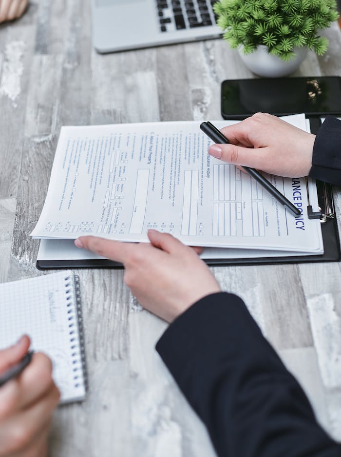 our-story Close-up of hands analyzing insurance policy paperwork with pen on table.